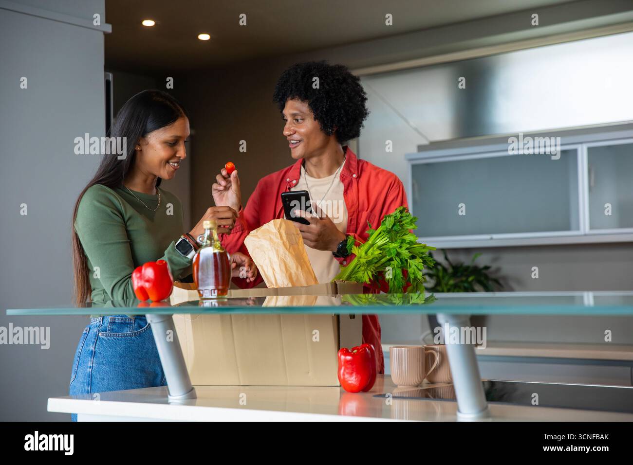 Couple afro-américain et indien déballage de l'épicerie dans la cuisine avec sac d'épicerie, smartphone Banque D'Images Couple afro-américain et indien déballage de l'épicerie dans la cuisine avec sac d'épicerie, smartphone Banque D'Images