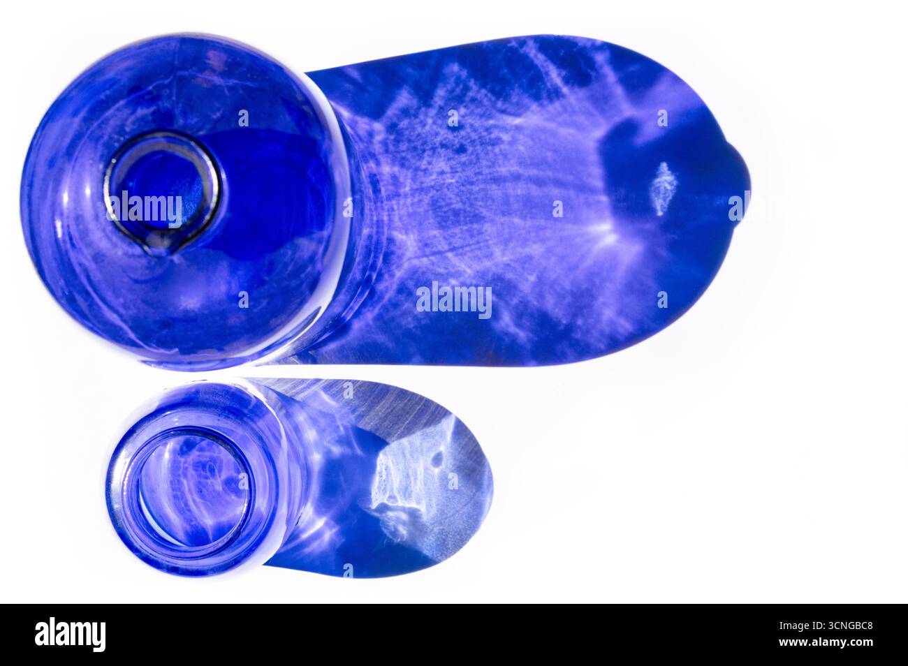 Vue de dessus de deux vases en verre bleu projetant une réflexion bleue sur fond blanc Banque D'Images