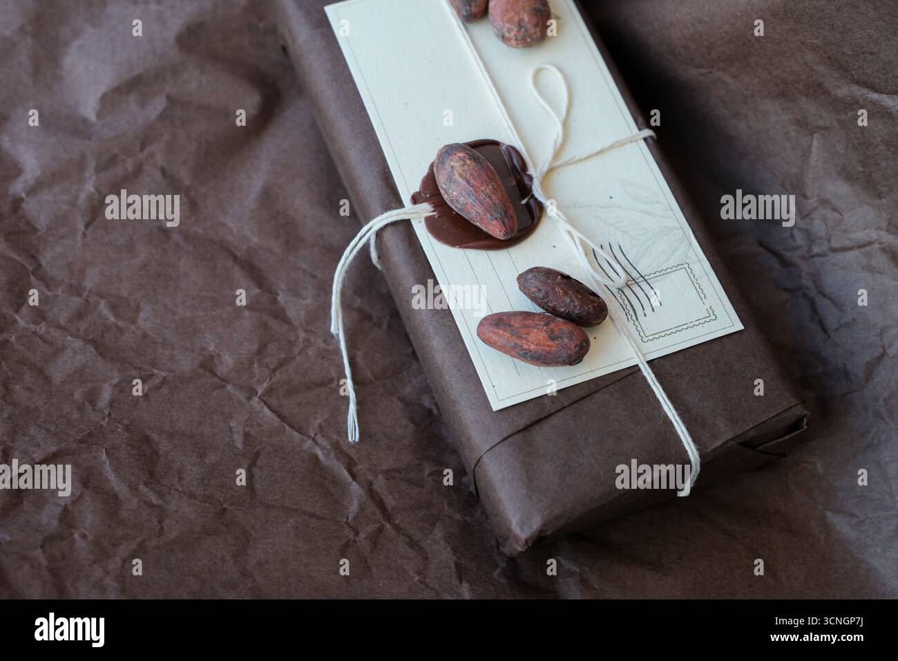 Colis de chocolat avec cire à cacheter. Barres de chocolat cadeau dans un emballage brun sur papier d'emballage froissé brun. Fèves de cacao. Banque D'Images