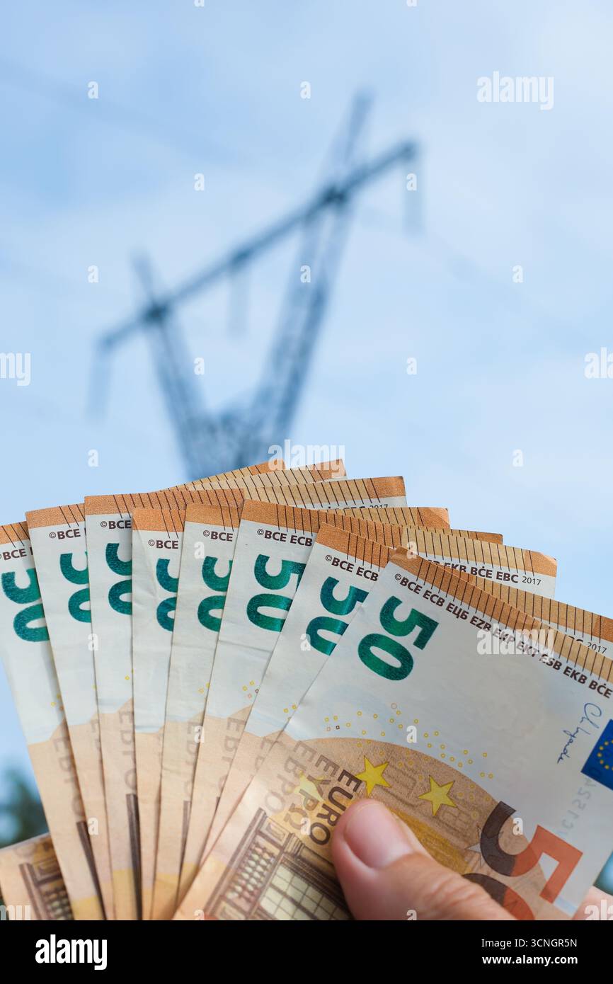 Personne détenant un éventail de billets en euros sur fond de tour d'électricité. Fond de ciel bleu. Banque D'Images