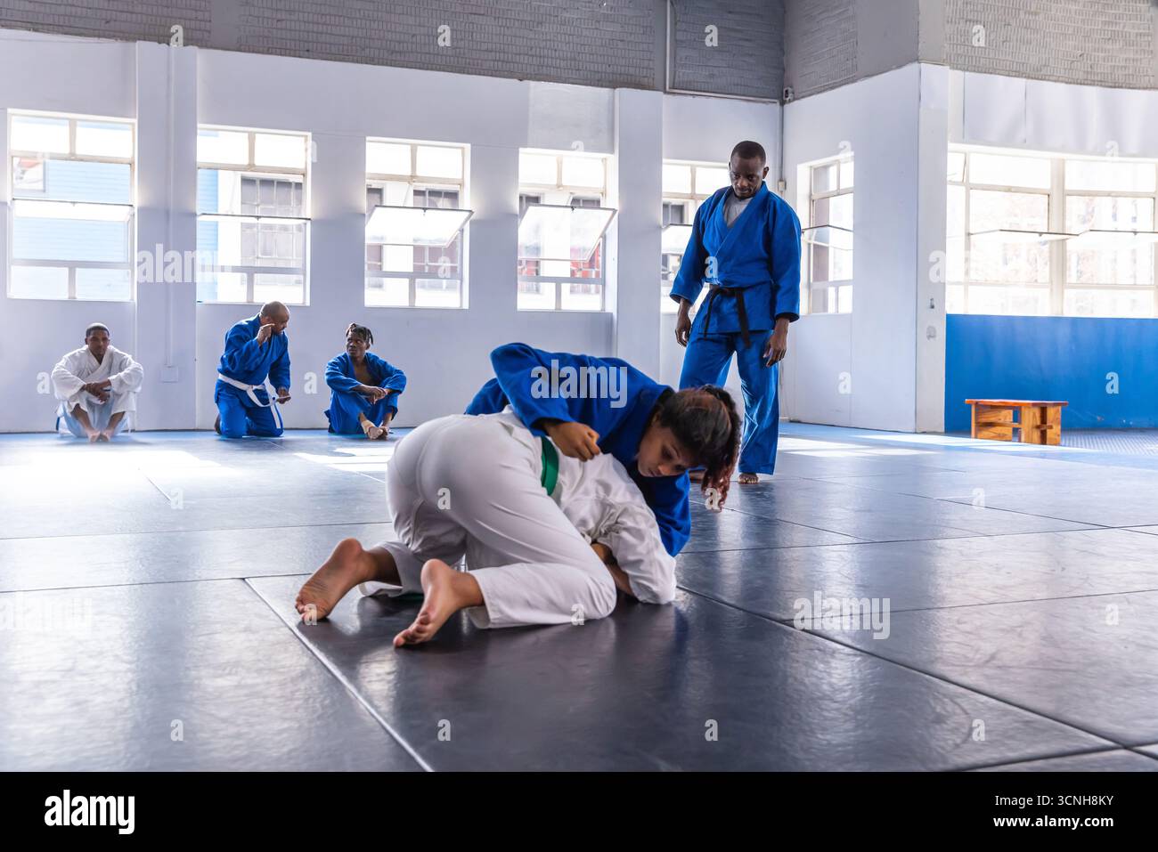 Partenaires de sparring adolescentes luttant dans sig sur des tapis dans le dojo sous la supervision de l'instructeur Banque D'Images