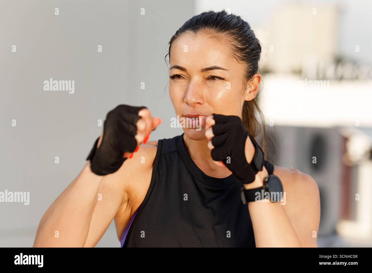 Jeune femme en posture de combat, prête pour la boxe d'ombre. Portrait d'une jeune femme mince portant des gants de fitness debout à l'extérieur. Banque D'Images