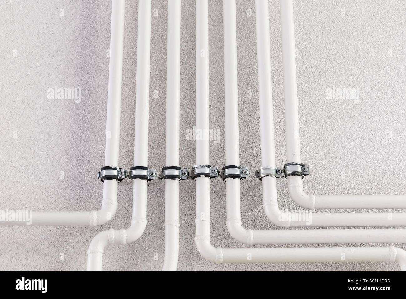 Tuyaux en plastique blanc reliés à un mur blanc avec des pinces métalliques robustes, formant un système de plomberie profilé pour une distribution efficace de l'eau Banque D'Images