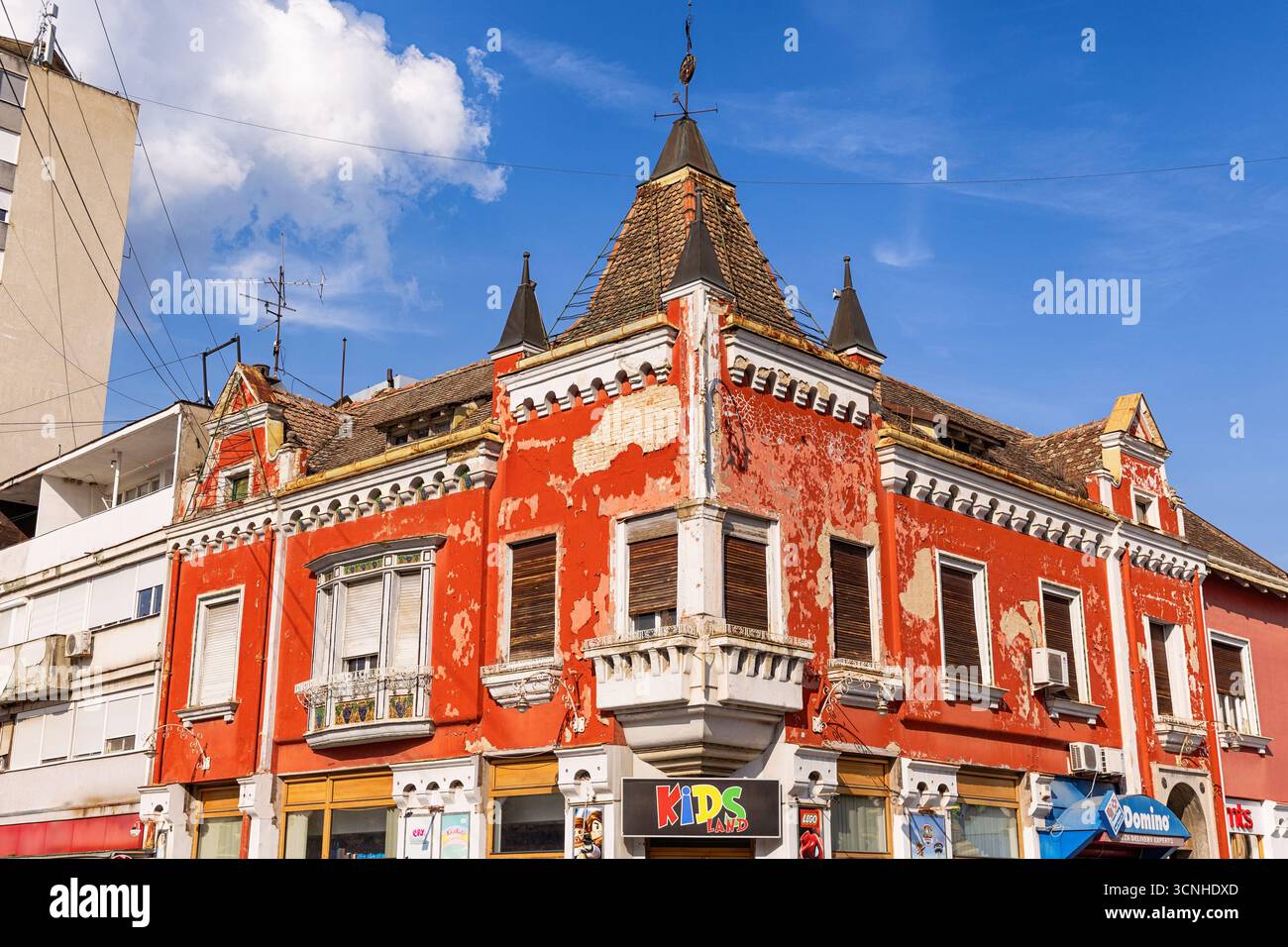 3 août 2025, Vrsac, Serbie : vue en angle bas d'un vieux bâtiment rouge délabré avec de petites tourelles, de la peinture écaillée et des volets fermés Banque D'Images