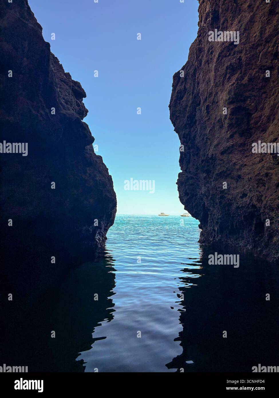Vue sur la mer à travers une grotte côtière s'ouvrant avec de l'eau bleue claire et des bateaux au loin. Banque D'Images