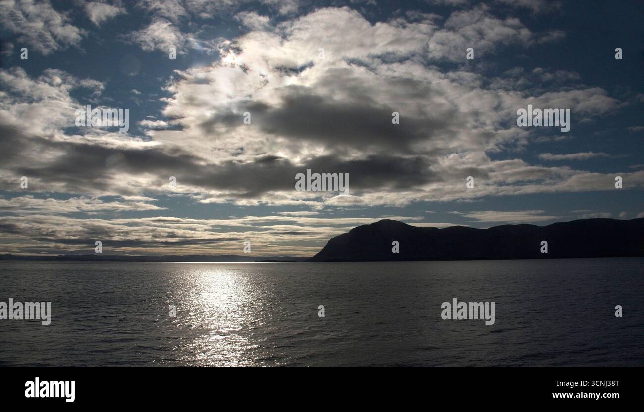 La lumière du soleil se reflète sur la surface de l'eau dans la baie des îles de Terre-Neuve alors que les nuages dérivent au-dessus. Une silhouette de montagne ajoute de la profondeur aux terres sereines Banque D'Images