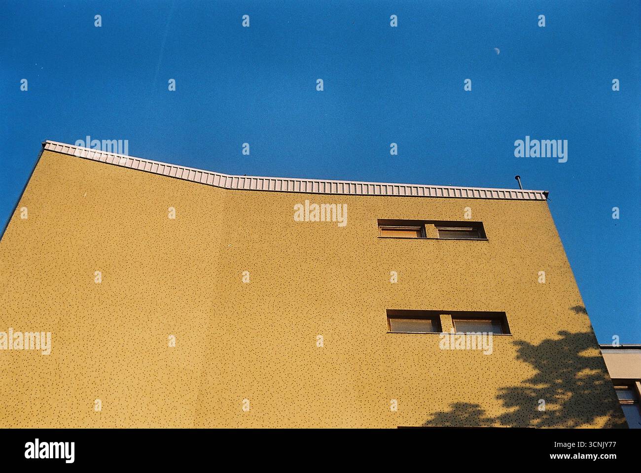 Photographie analogique d'un mur de bâtiment en mosaïque jaune des années 1960, contrastant avec un ciel bleu clair. Une vue d'archives tranquille de milieu du siècle urbain Banque D'Images