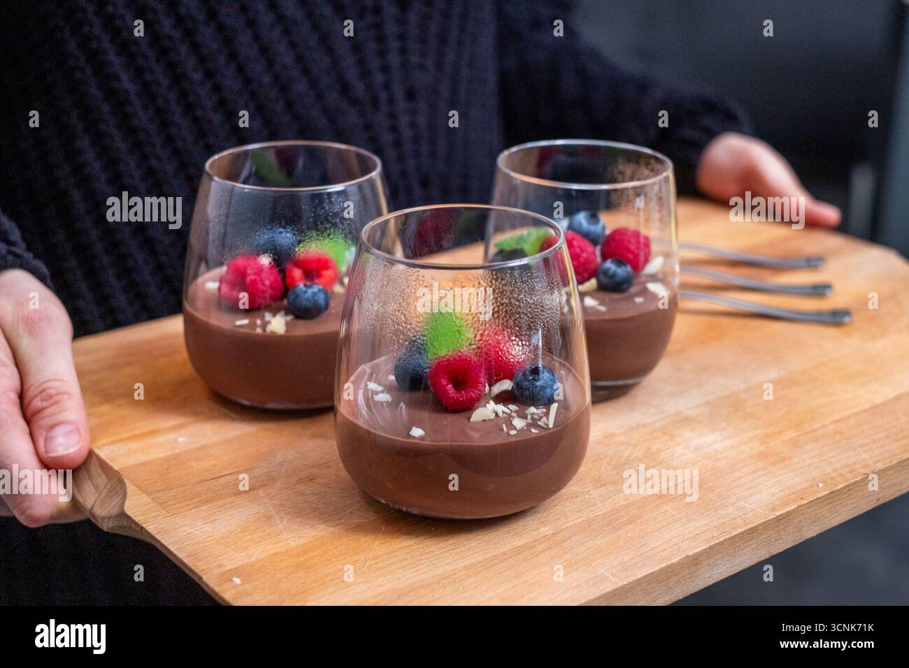 Dessert au chocolat dans des verres élégants, garni de baies, servi sur plateau en bois, mettant en valeur la présentation gourmande et l'atmosphère accueillante Banque D'Images