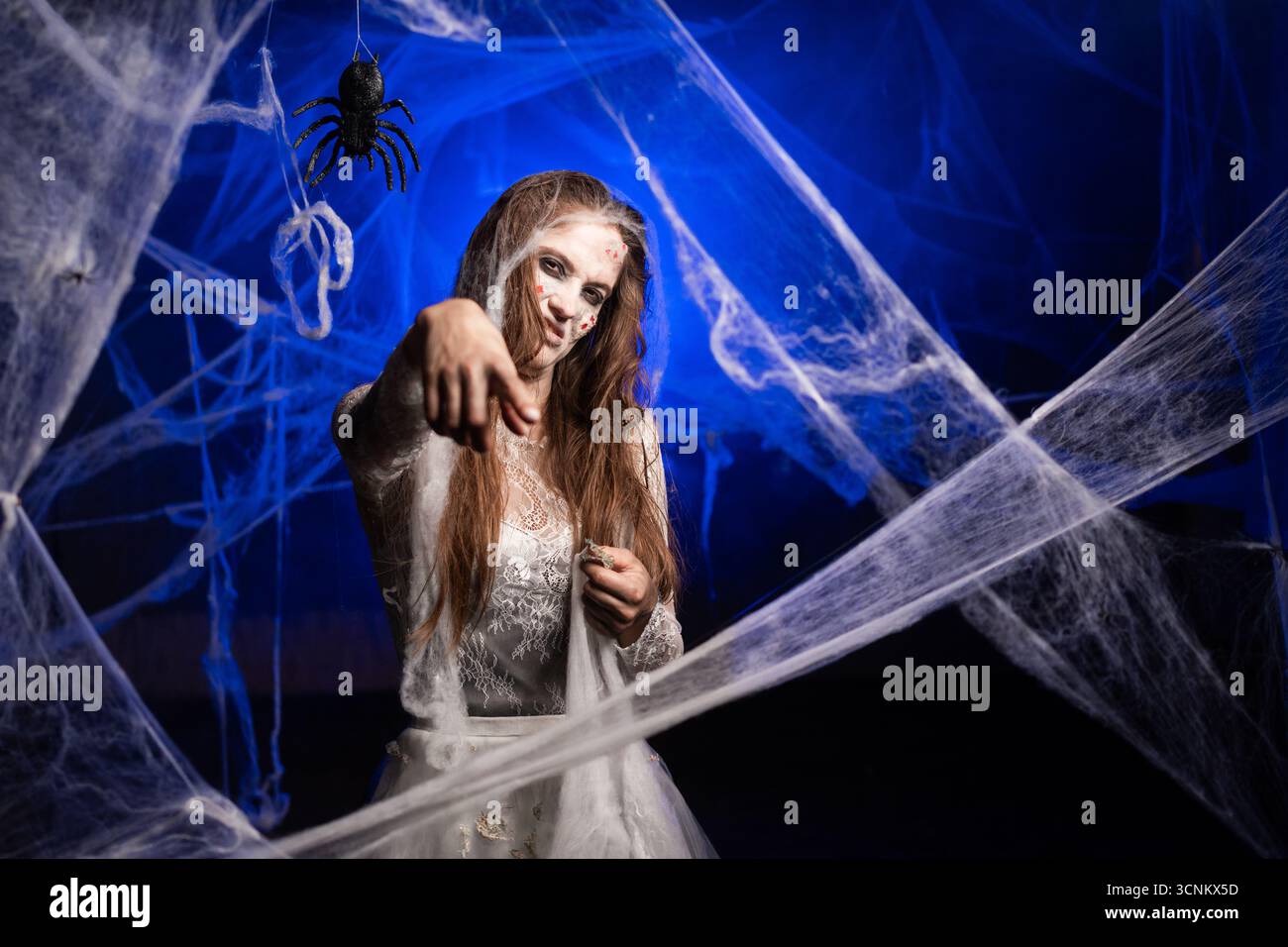 Sinistre femme avec le maquillage zombie effrayant Halloween pointant l'index à la caméra disent que nous avons besoin de vous. essayant d'effrayer. Fille morte avec des cicatrices visage sur bleu Banque D'Images