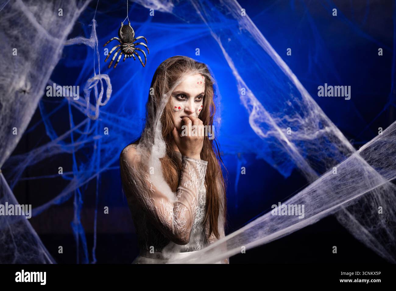 Femme sinistre avec le maquillage zombie effrayant Halloween éprouvant des ongles mordus de paranoïa souffrant d'émotion de stress. Fille morte avec des cicatrices visage sur araignée bleue Banque D'Images