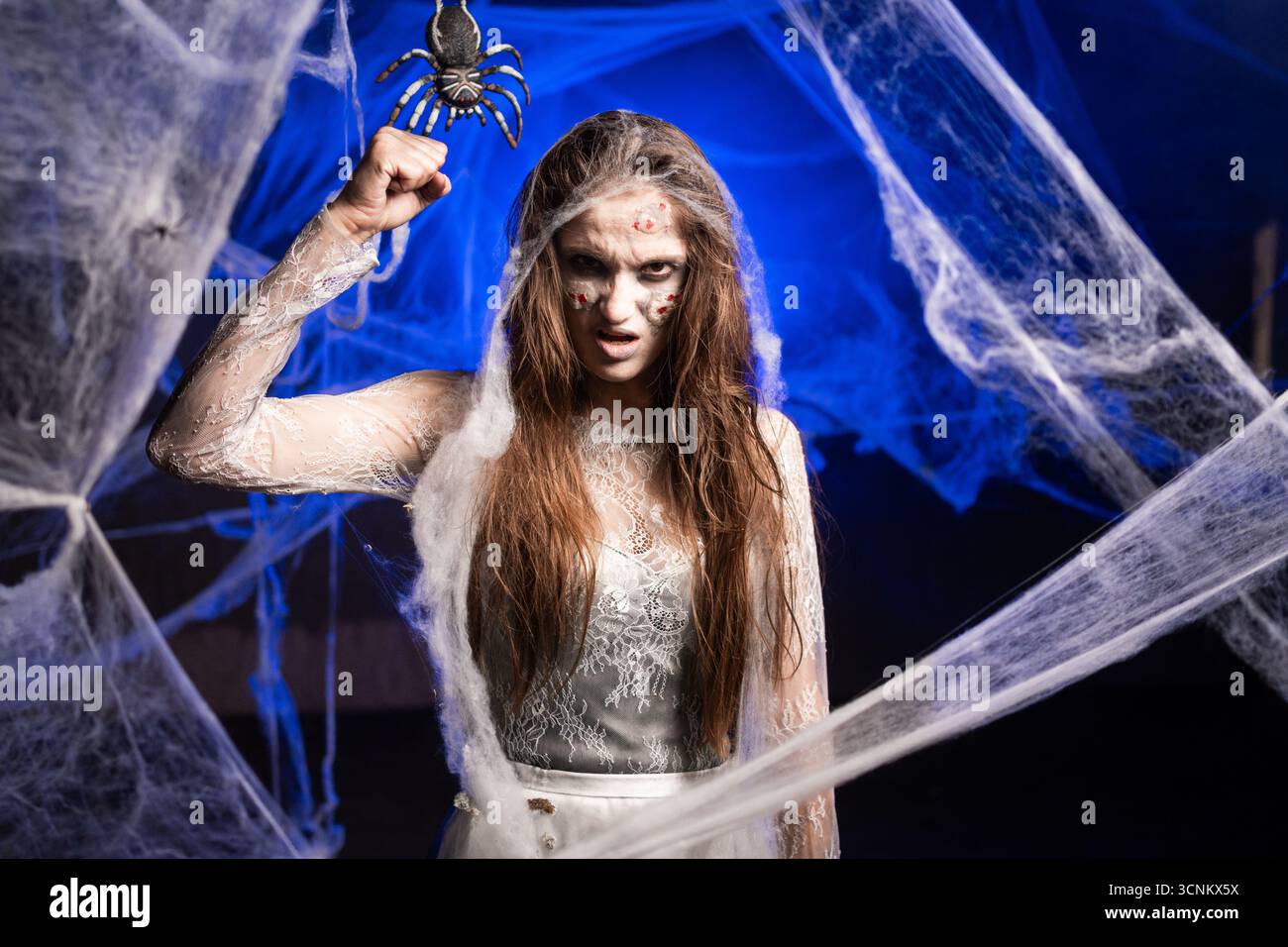 Sinistre femme avec le maquillage zombie effrayant Halloween tenant le geste de frappe poing-up à la caméra essayant de faire peur. Les cicatrices de dame morte font face sur des toiles d'araignées backgro Banque D'Images