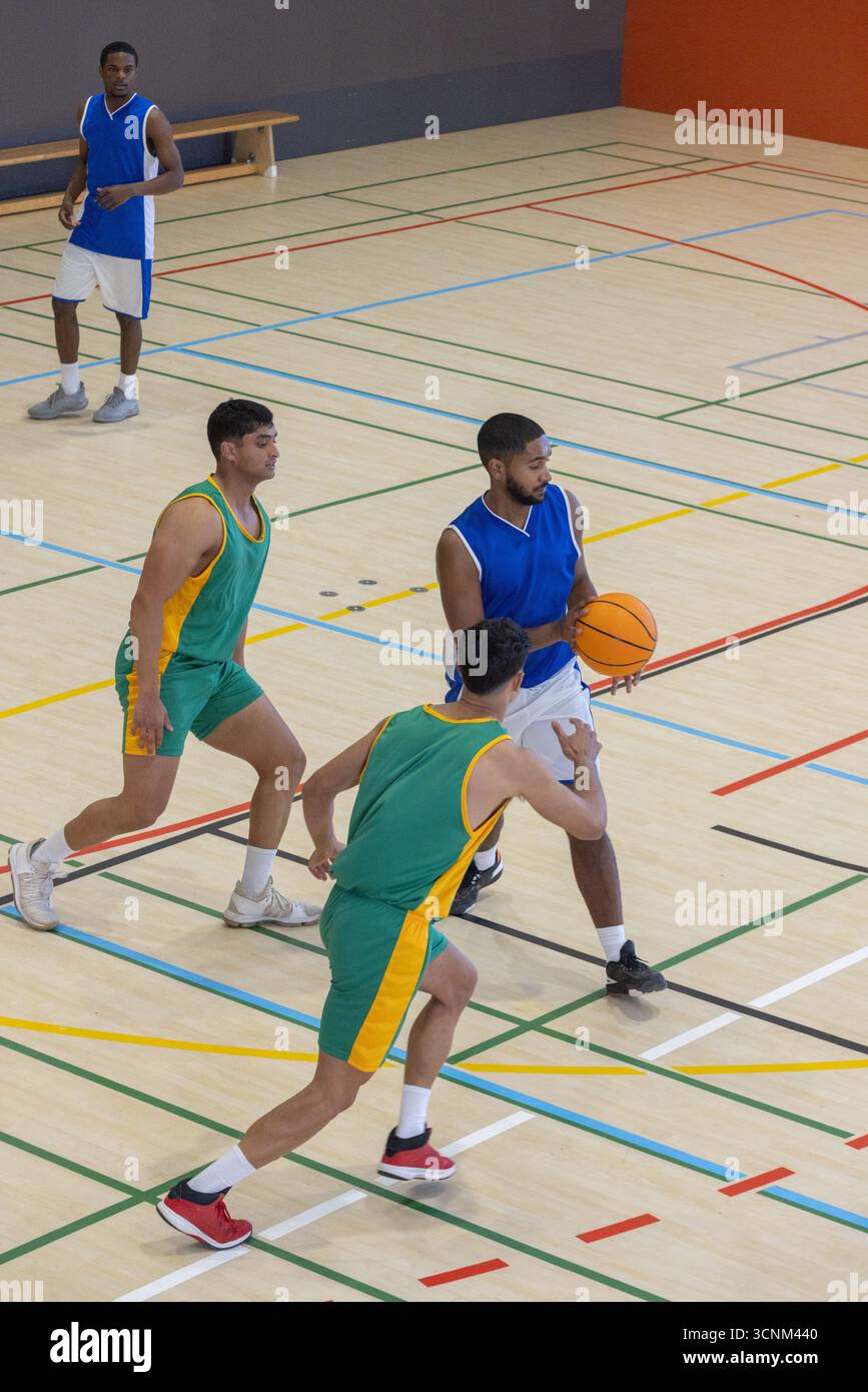 Homme afro-américain dribble basket-ball en uniforme bleu sur un court en bois marqué de lignes Banque D'Images