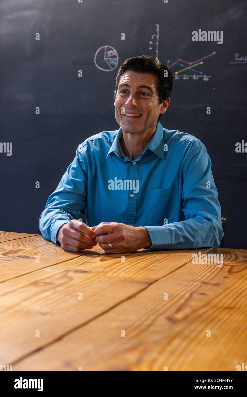 Conférencier masculin présentant en classe avec table et tableau noir avec graphiques à secteurs et linéaires Banque D'Images