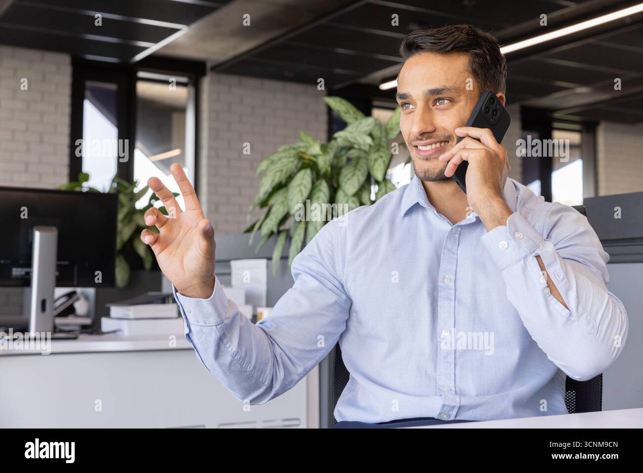 Homme indien parlant sur smartphone, geste OK au bureau avec des moniteurs dans le bureau, espace de copie Banque D'Images