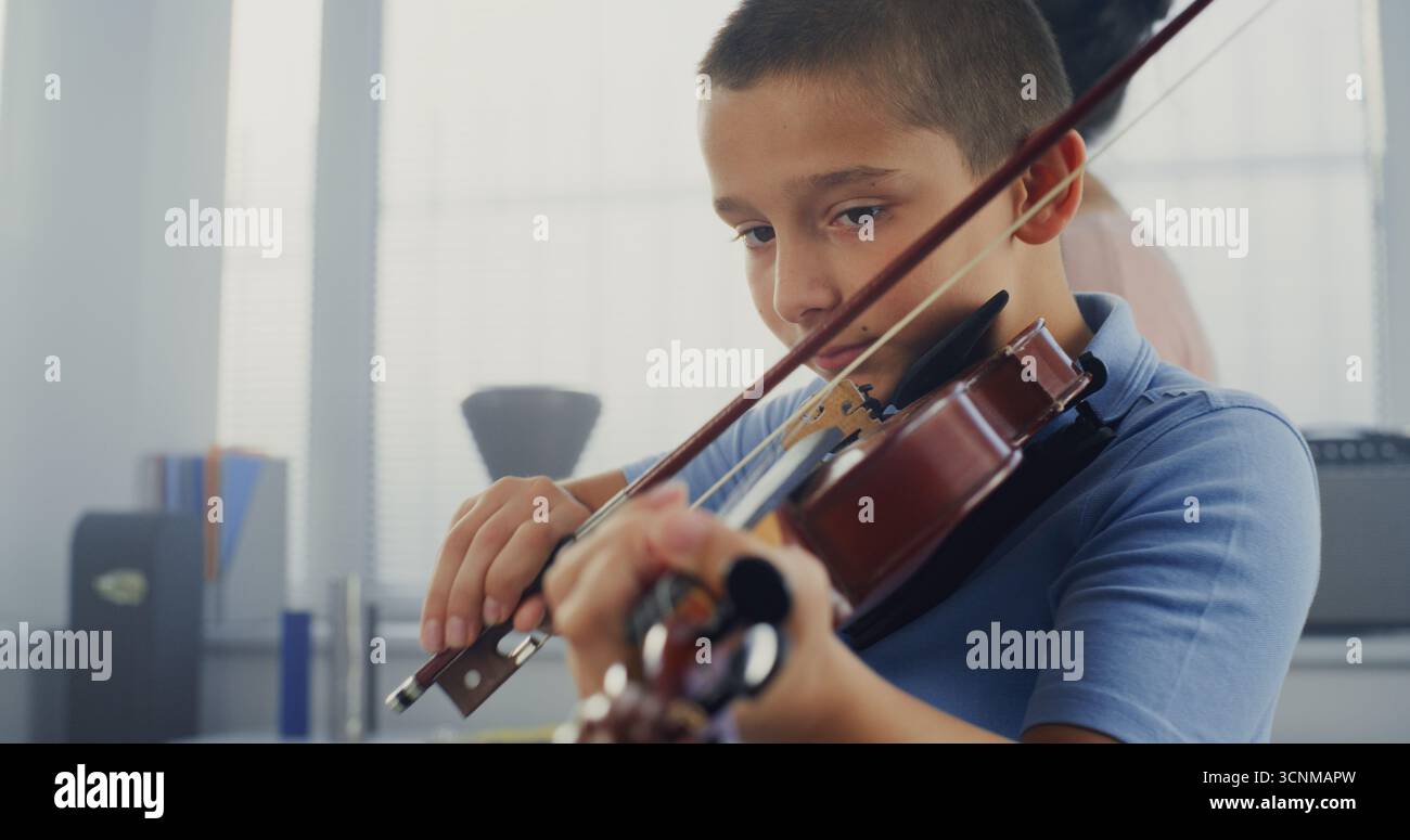 Garçon de l'école primaire pratiquant le violon en classe de musique, rêvant de devenir musicien. Enseignant guidant l'enfant artistique en jouant un instrument de musique. Éducation musicale, leçon de violon, répétition. Banque D'Images