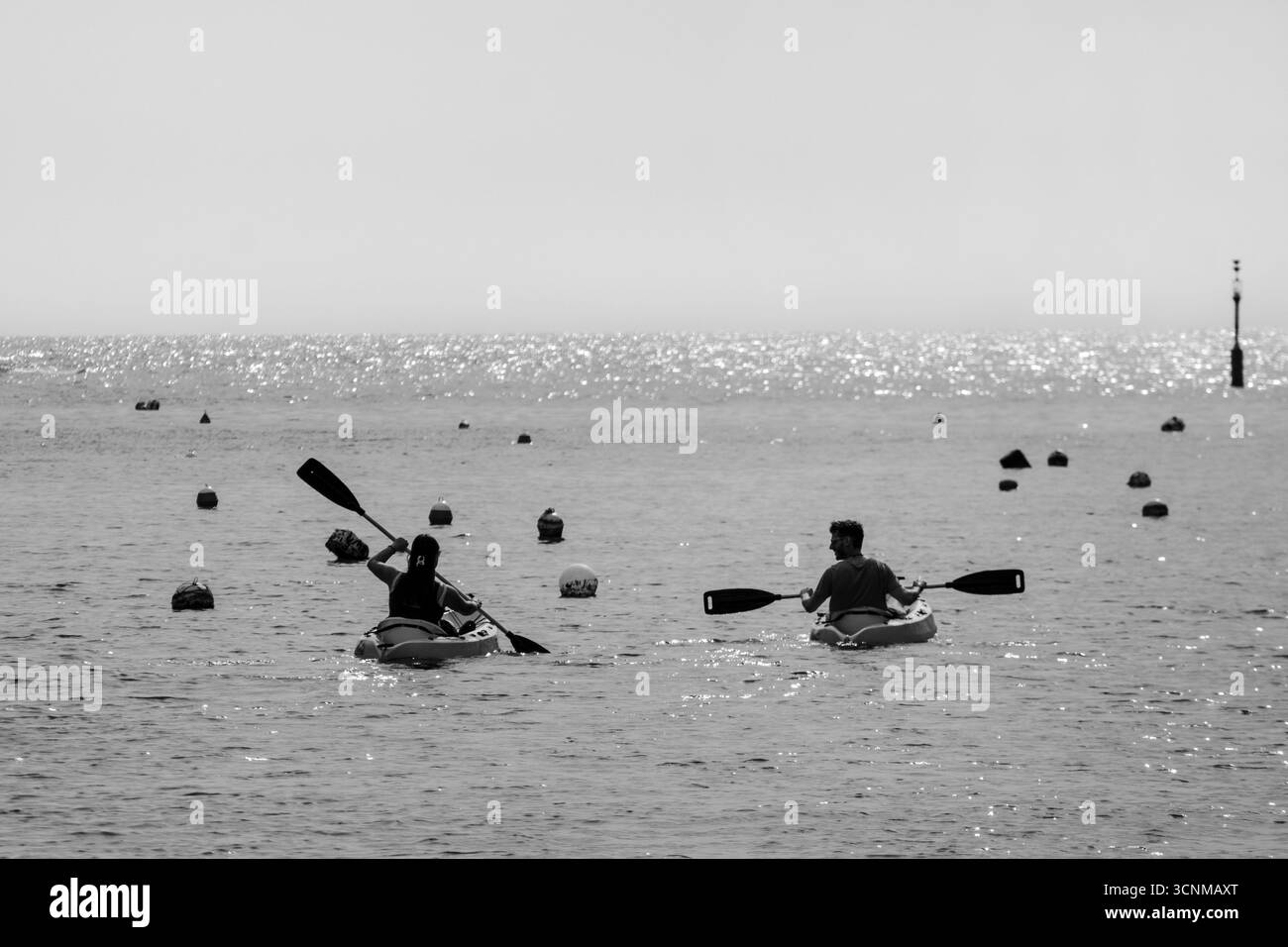 Xlendi, Gozo, Malte - 12 avril 2025 : deux personnes faisant du kayak sur une eau scintillante calme parmi les bouées flottantes sous le soleil de l'après-midi Banque D'Images
