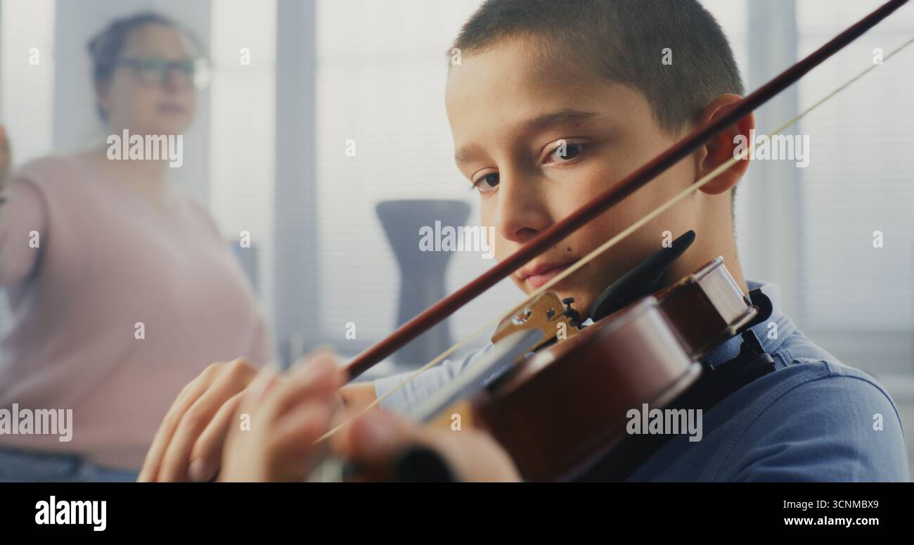Gros plan sur un garçon talentueux jouant du violon pendant la leçon de musique, répétant avant la performance musicale. Enseignant soutenant et enseignant futur musicien. Éducation musicale, cours de pratique du violon à l'école. Banque D'Images