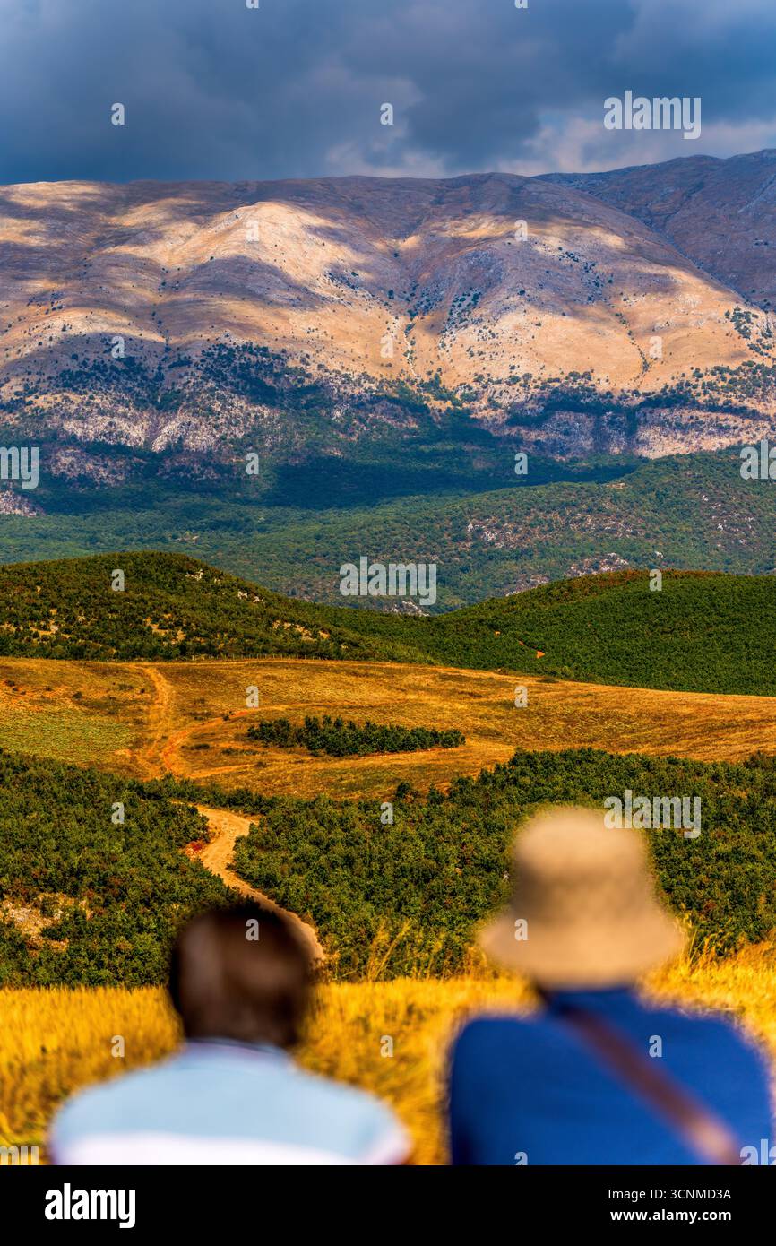 Deux voyageurs admirant la beauté pittoresque de la montagne sèche (Mali i Thatë) à Pogradec, Albanie – champs dorés, collines verdoyantes et pics dramatiques Banque D'Images