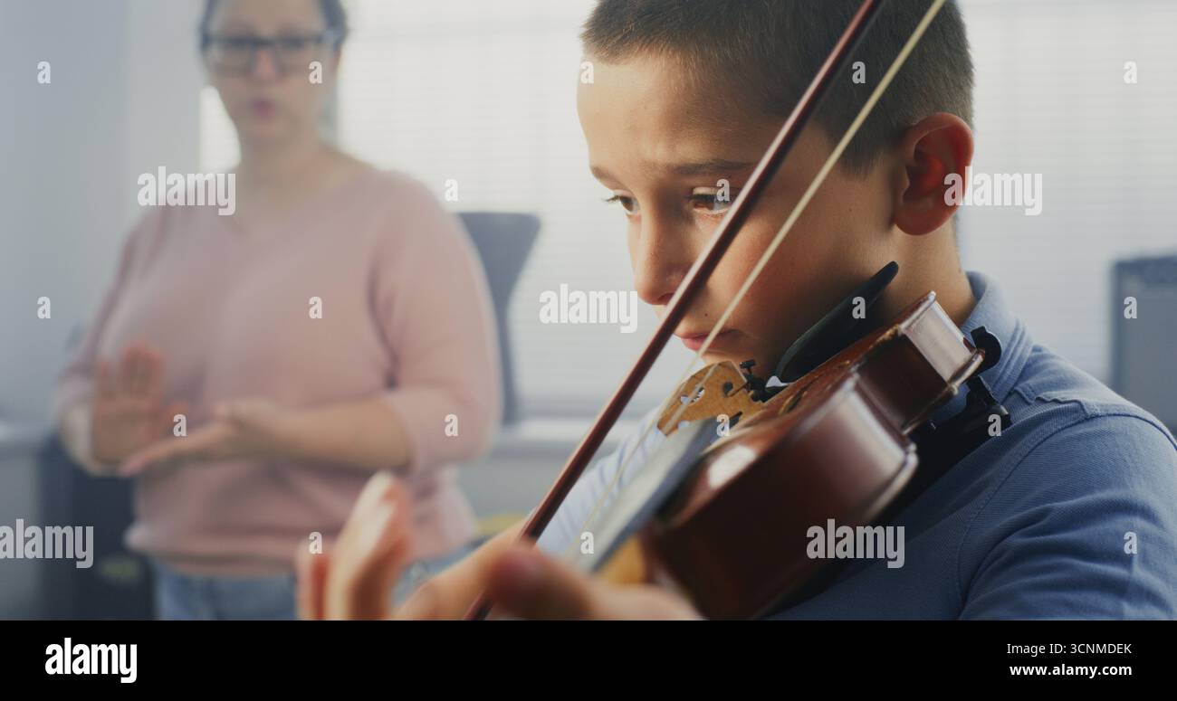 Gros plan sur un garçon talentueux jouant du violon pendant la leçon de musique, répétant avant la performance musicale. Enseignant soutenant et enseignant futur musicien. Éducation musicale, cours de pratique du violon à l'école. Banque D'Images
