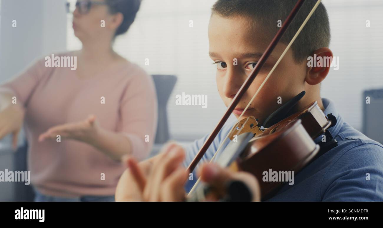 Gros plan sur un garçon talentueux jouant du violon pendant la leçon de musique, répétant avant la performance musicale. Enseignant soutenant et enseignant futur musicien. Éducation musicale, cours de pratique du violon à l'école. Banque D'Images