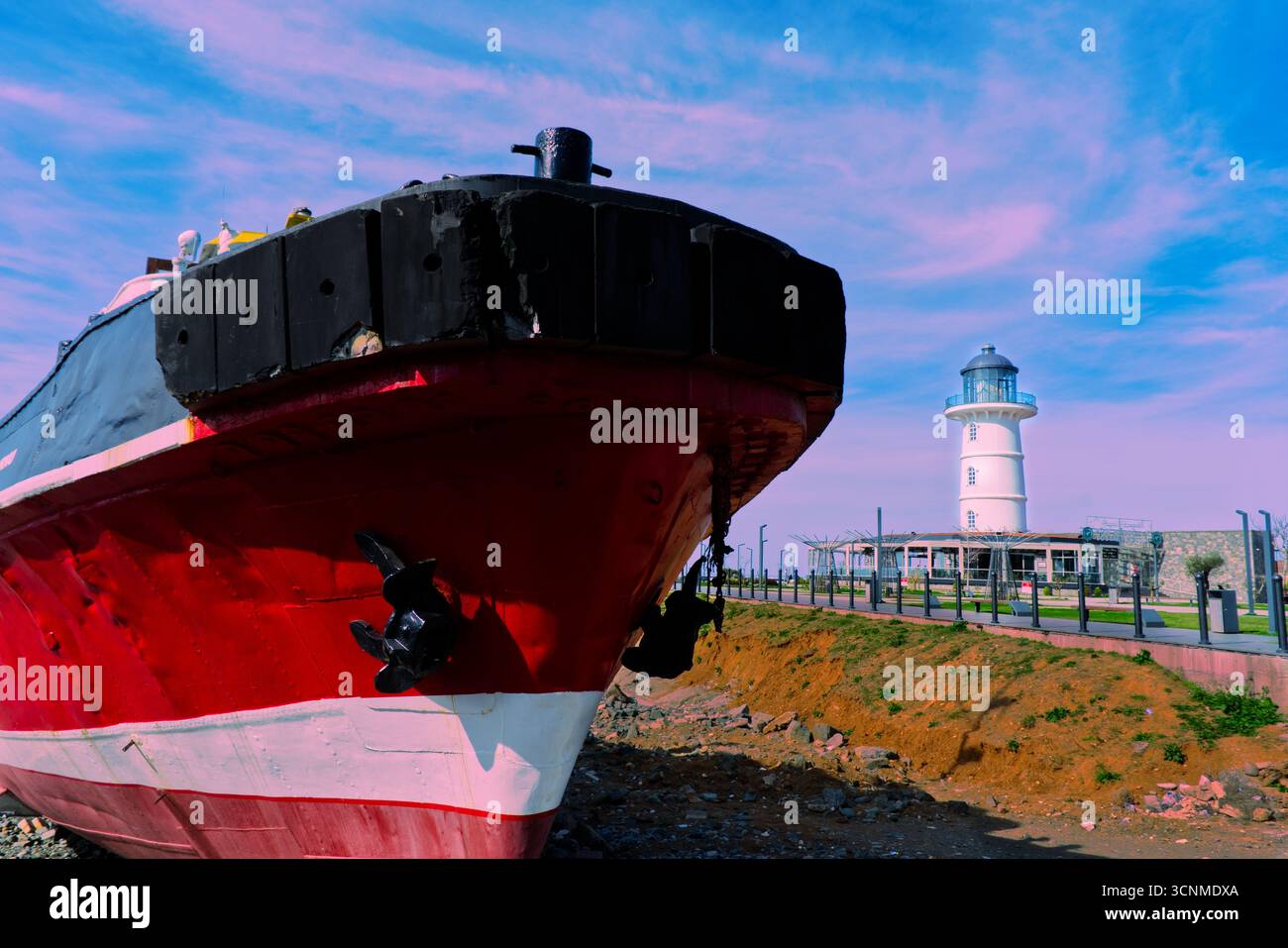 Red and Black Ship accosté près du phare blanc. Un navire rouge et noir saisissant est amarré près d'un phare blanc par une journée ensoleillée. Banque D'Images