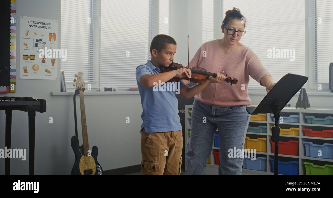 Garçon talentueux jouant du violon pendant la leçon de musique à l'école primaire, répétant avant la performance musicale. Enseignant soutenant et enseignant futur musicien. Éducation musicale, cours de pratique du violon. Banque D'Images