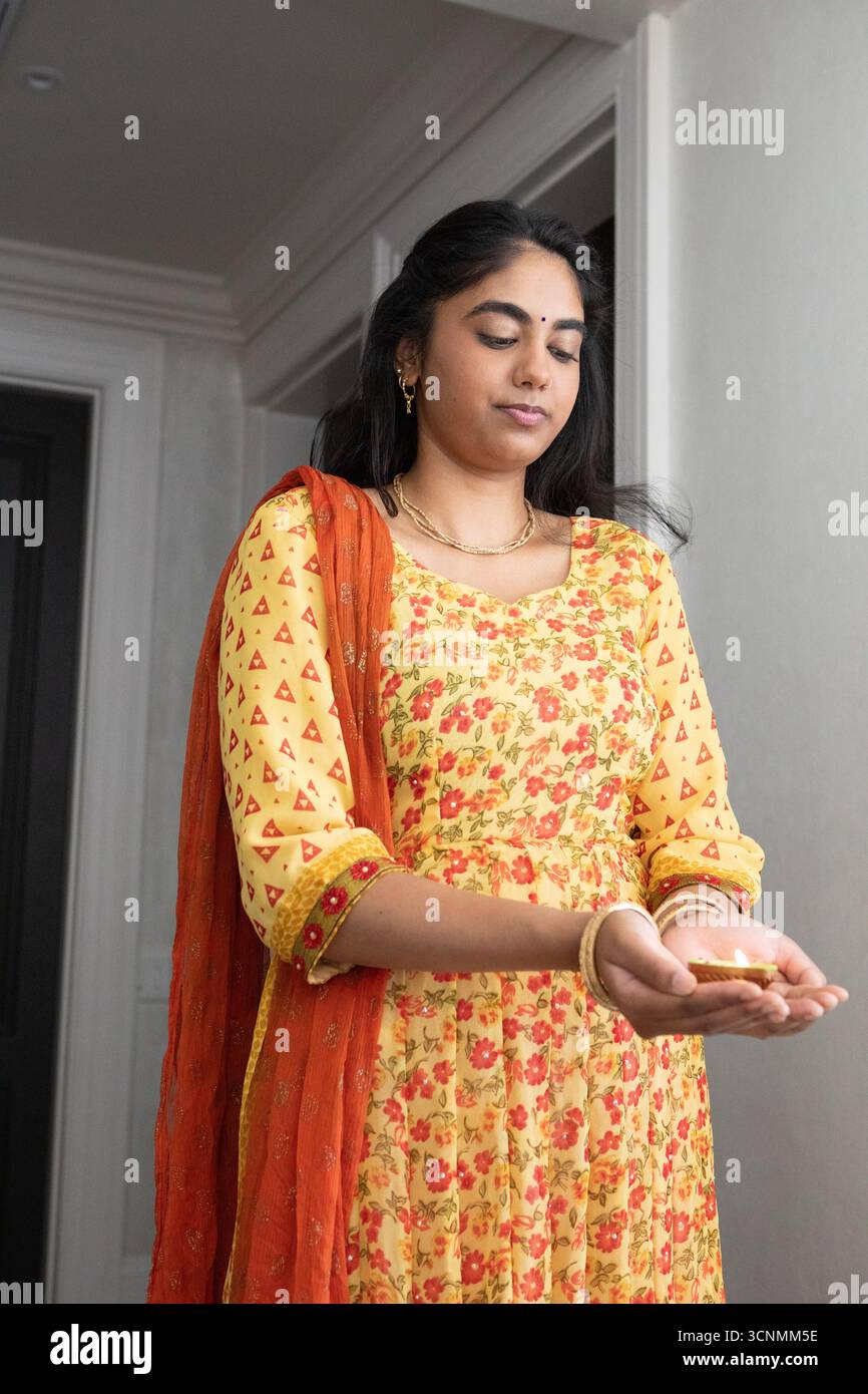 Femme indienne portant kurta floral et dupatta, tenant un objet métallique dans le couloir avec des bijoux en or Banque D'Images