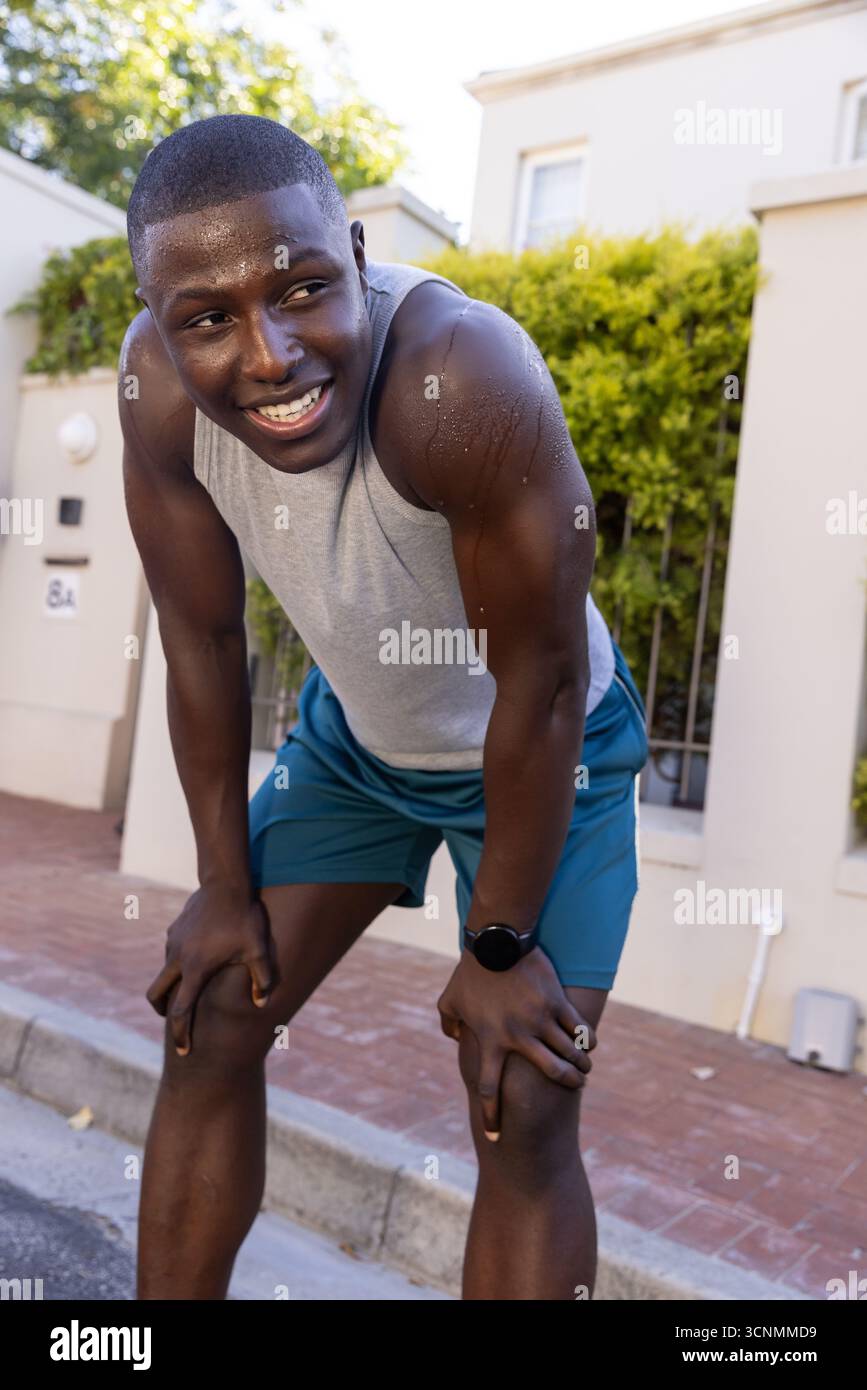 Homme afro-américain vérifiant la montre de sport s'arrêtant sur le trottoir de briques à côté de la haie, clôture de fer Banque D'Images