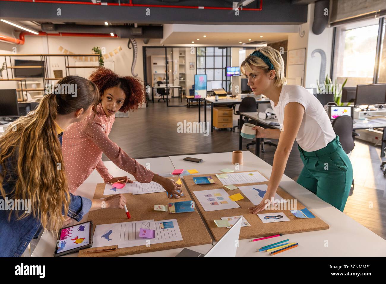 Diverses collègues féminines travaillant autour de la table de bureau avec des croquis, des tablettes et des notes autocollantes Banque D'Images