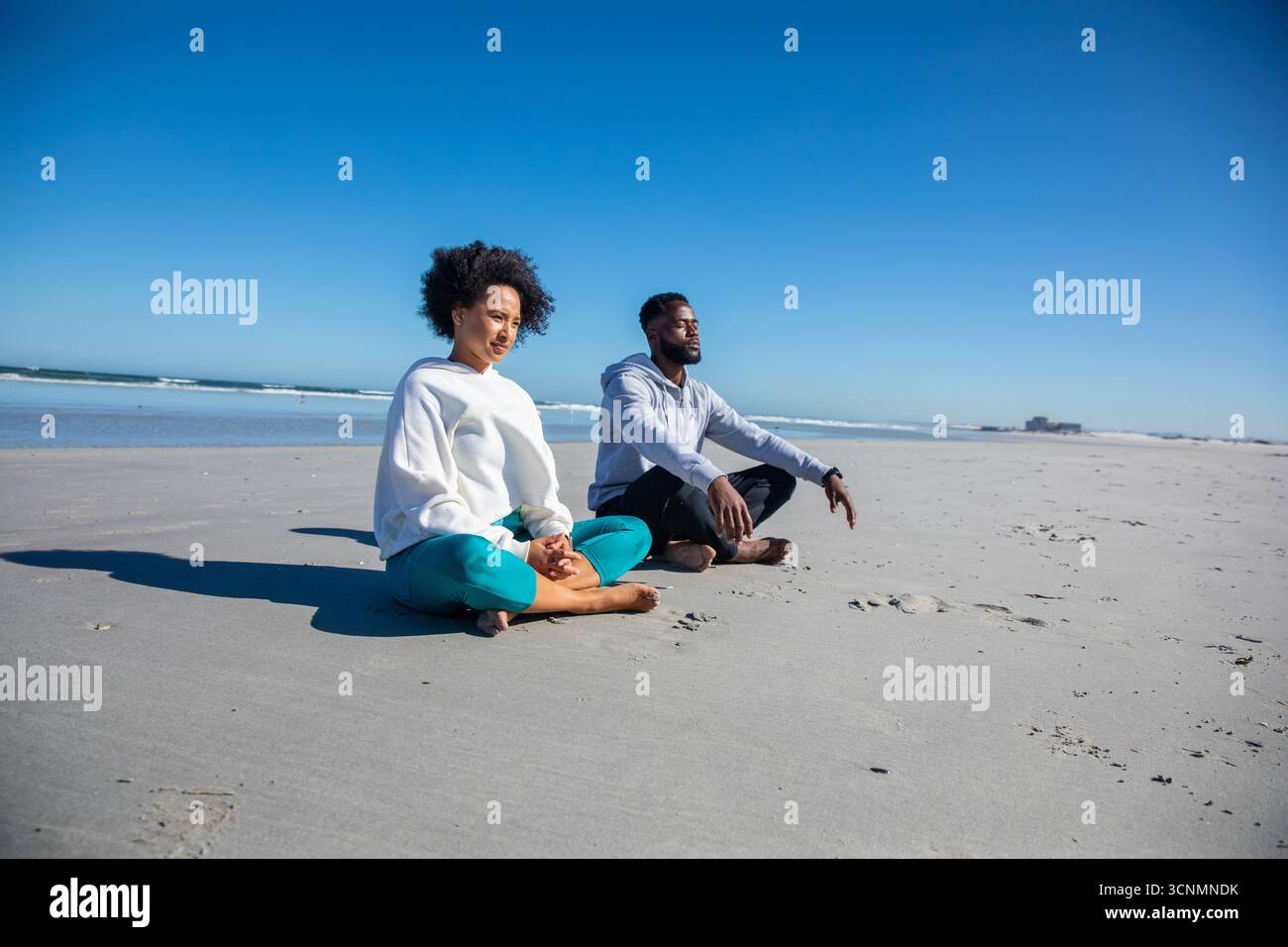 Divers amis croisés sur le rivage sablonneux de l'océan pratiquant la méditation, espace de copie Banque D'Images