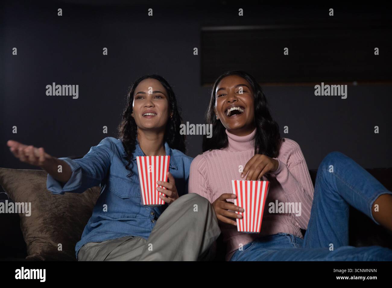 Diverses amies féminines assises sur un canapé en peluche dans le salon avec des seaux à pop-corn et réagissant Banque D'Images Diverses amies féminines assises sur un canapé en peluche dans le salon avec des seaux à pop-corn et réagissant Banque D'Images