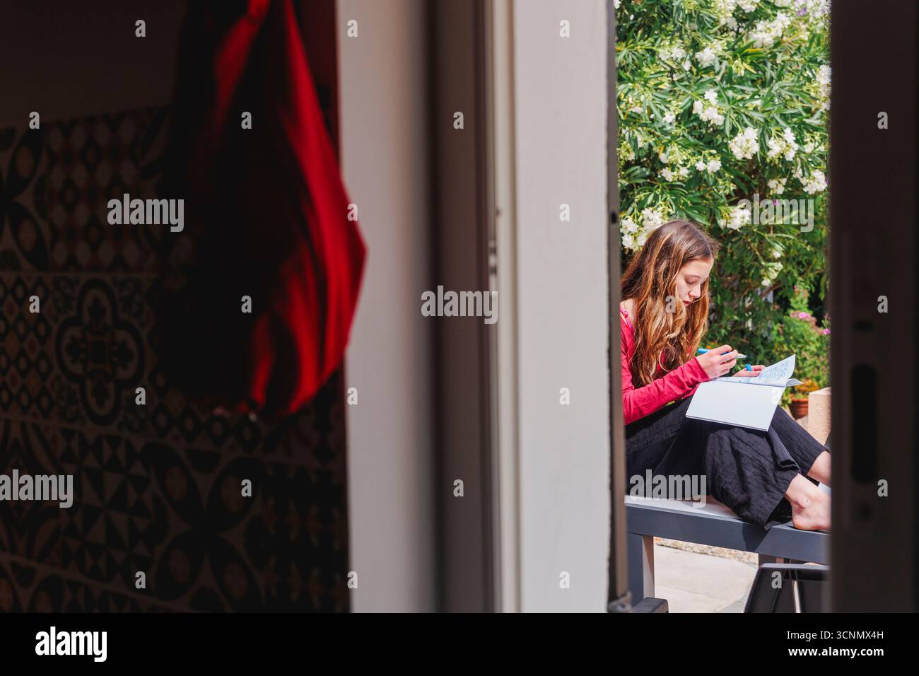 Vue par la fenêtre de la fille assise dans le jardin écrivant dans le journal Banque D'Images