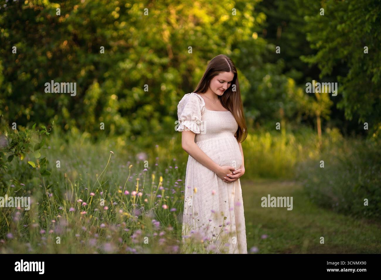 une mère maternelle brillante regarde son ventre de bébé dans un champ Banque D'Images