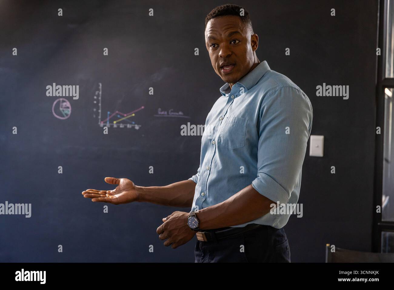 Homme afro-américain faisant des gestes à des dessins au tableau noir dans la salle de classe, espace de copie Banque D'Images