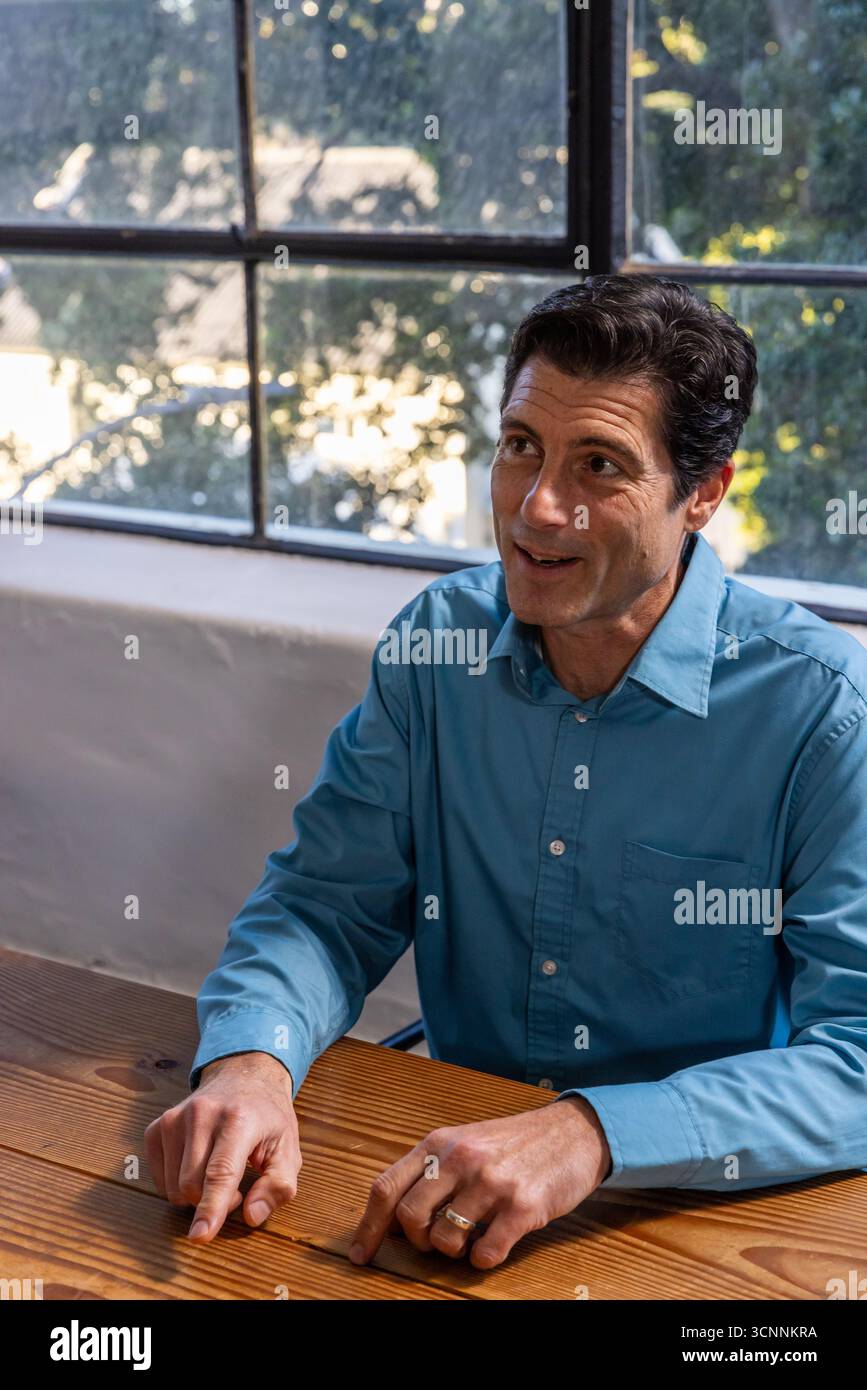 Homme portant une chemise bleu clair pointant vers la table par une grande fenêtre, espace de copie Banque D'Images