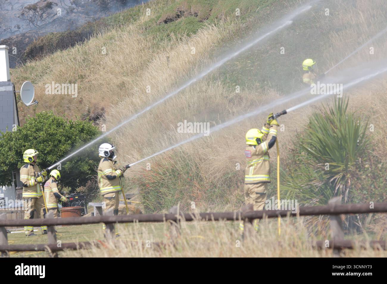 Cinq pompiers s'attaquent à la sécheresse de la propriété de chalet de vacances de plage sauvant les feux de forêt à Newgale, Pembrokeshire avec un mur d'eau de trois tuyaux. Banque D'Images
