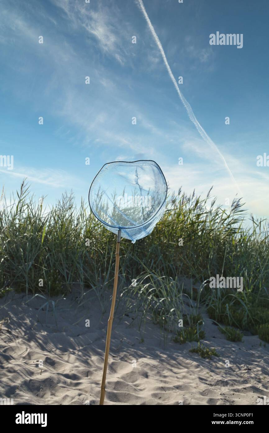 Un filet bleu avec un poteau en bois sur une plage de sable, avec un ciel bleu. Une dune avec de l'herbe derrière elle. Un sentiment de vacances. Un moment de calme dans la nature, avec de la lumière Banque D'Images