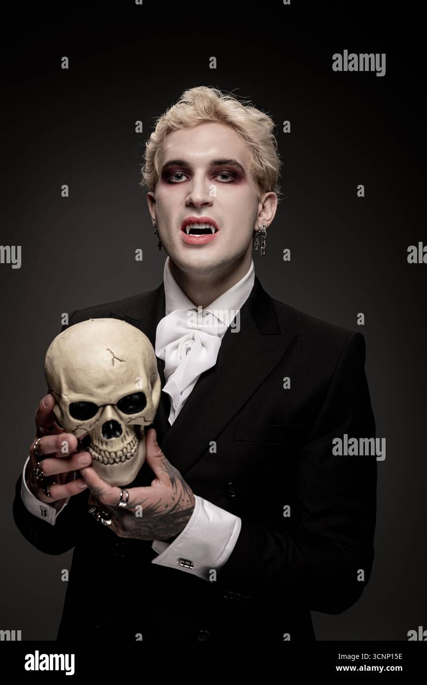 Young Man présente un impressionnant costume d'Halloween, tenant un crâne tout en étant habillé pour l'occasion. Banque D'Images
