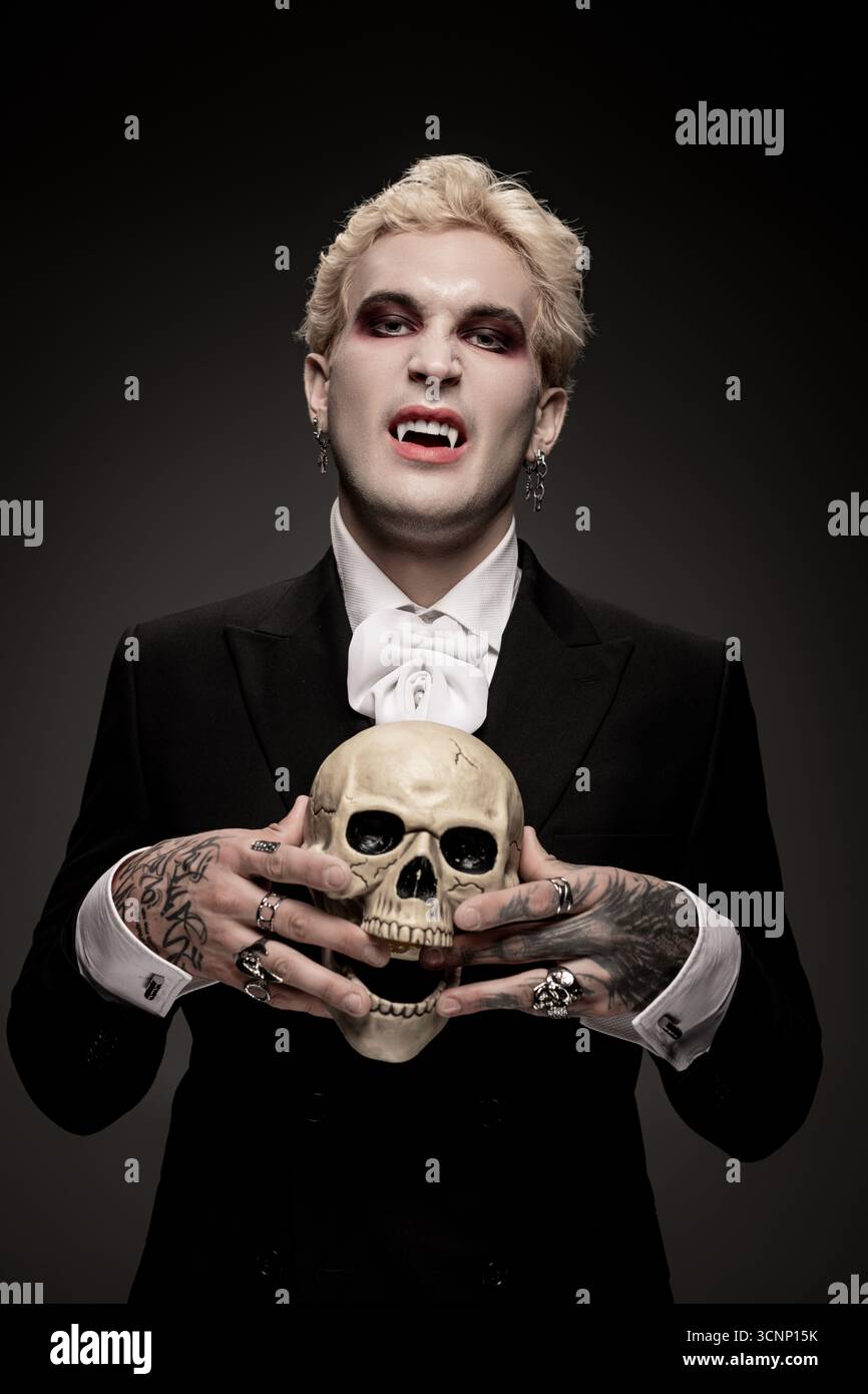 Un jeune homme beau vêtu d'un costume d'Halloween dramatique tient un crâne, mettant en valeur la créativité. Banque D'Images