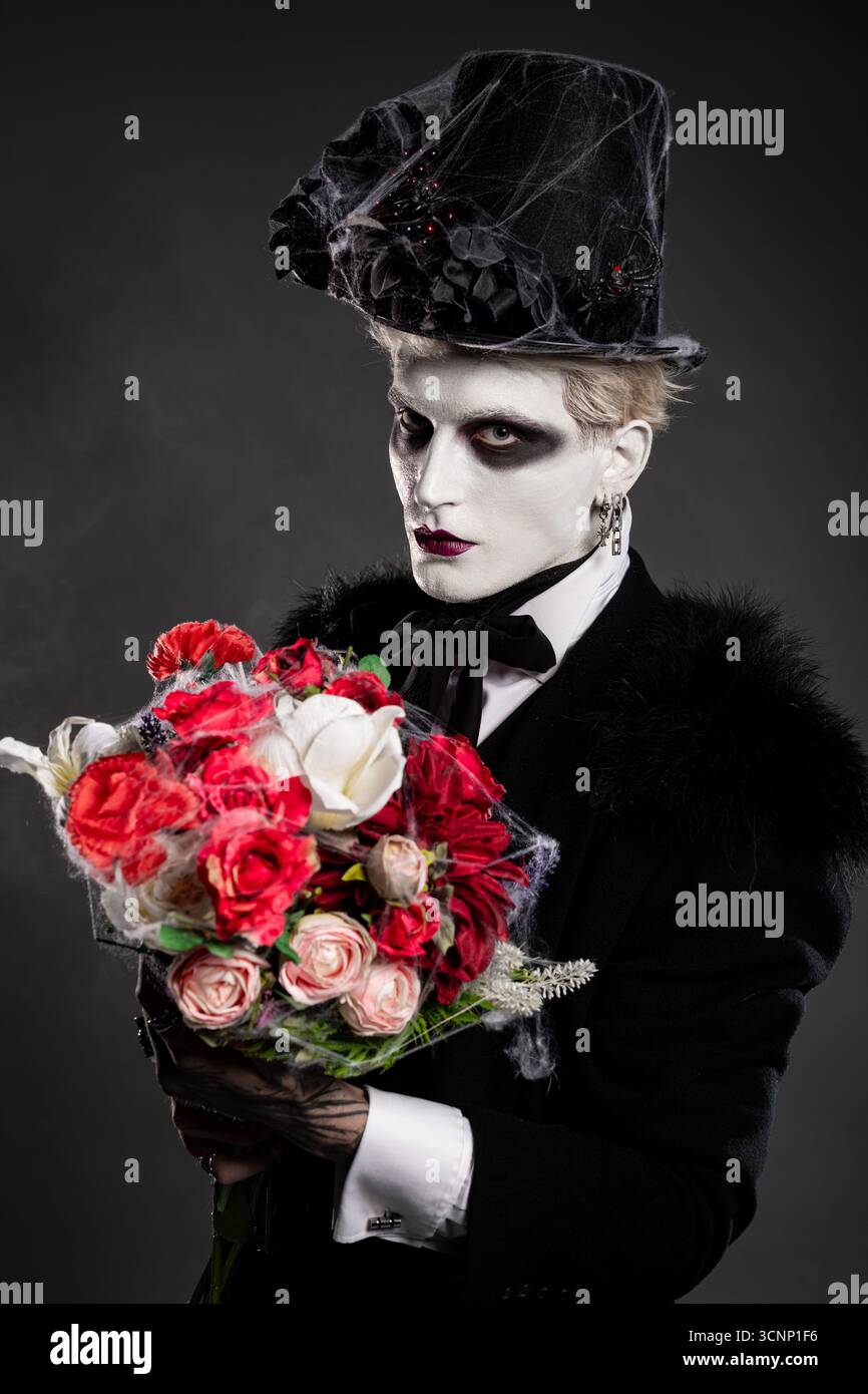 Jeune homme beau en costume d'Halloween frappant pose avec un bouquet de fleurs vibrantes. Banque D'Images