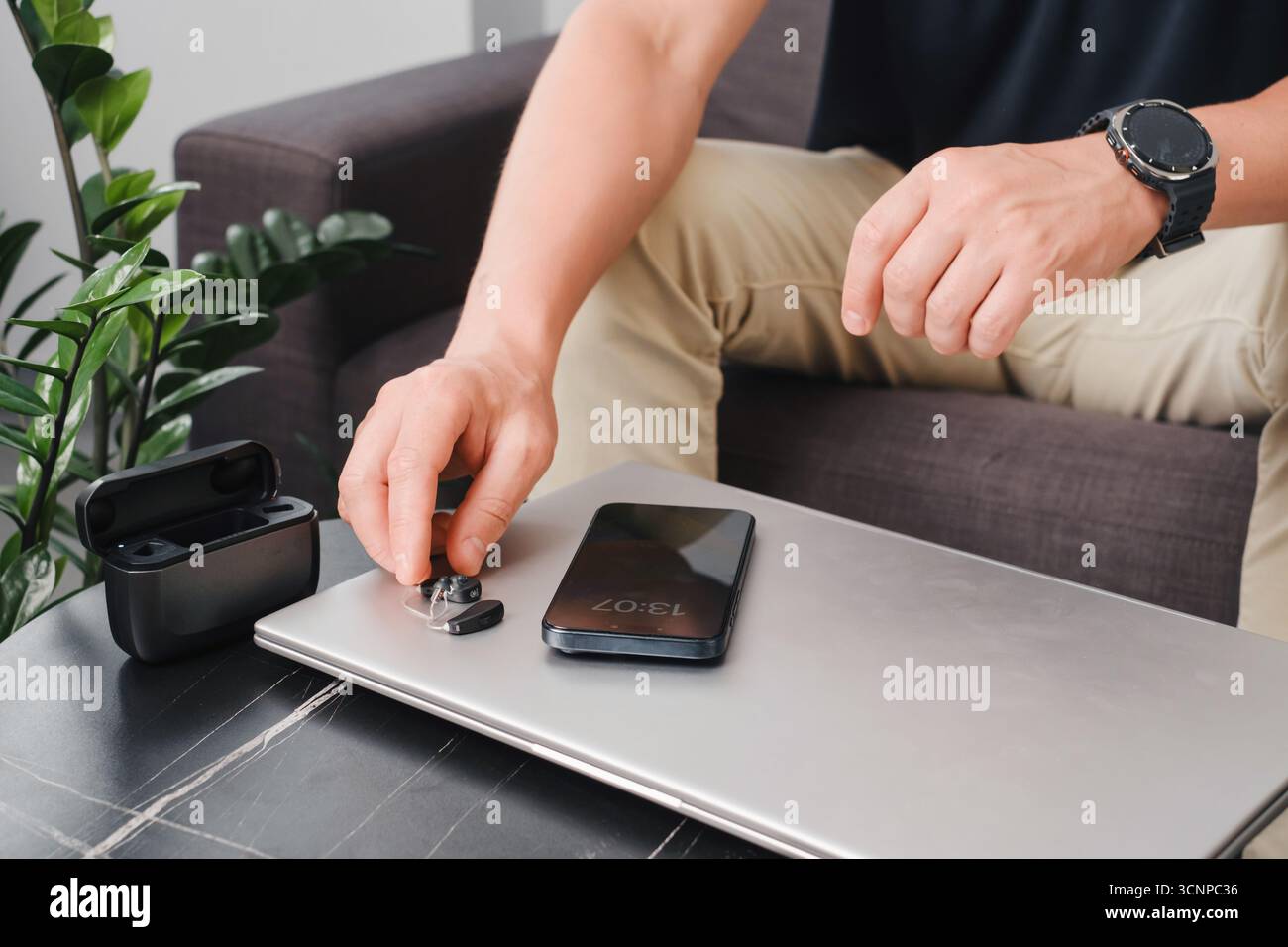 Aides auditives numériques modernes, smartphone et étui de chargement sur une table de bureau élégante, avec une personne préparant les appareils pour le travail. Environnement professionnel Banque D'Images