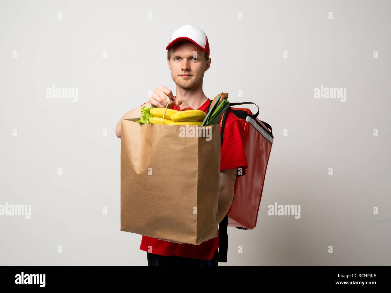 Coursier en uniforme rouge tenant le sac d'épicerie plein de fruits et légumes Banque D'Images