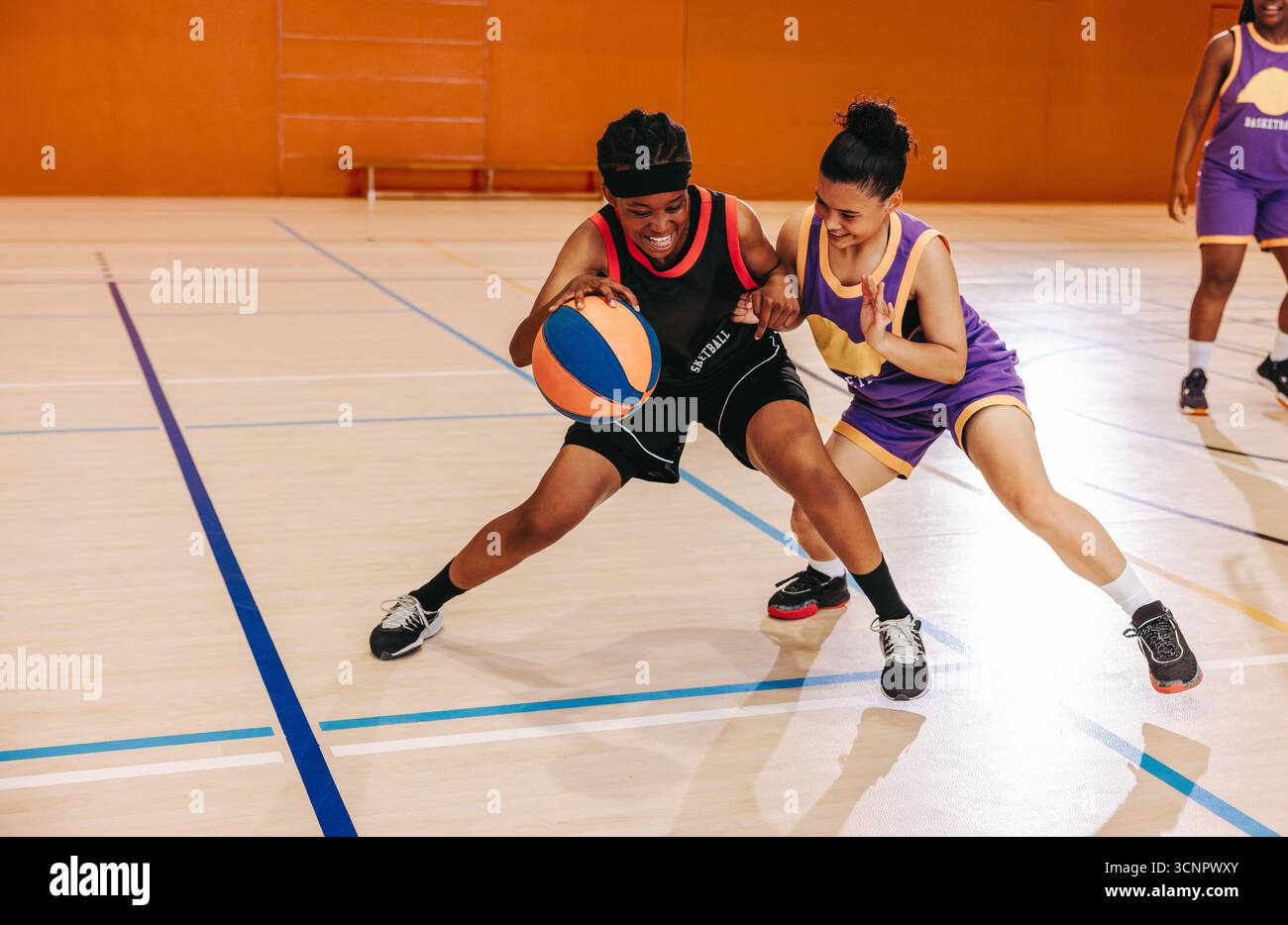 Deux jeunes femmes adultes en compétition active pour le basket-ball lors d'un match sportif au gymnase. Engagés dans un jeu disputé, les deux affichent des compétences athlétiques Banque D'Images