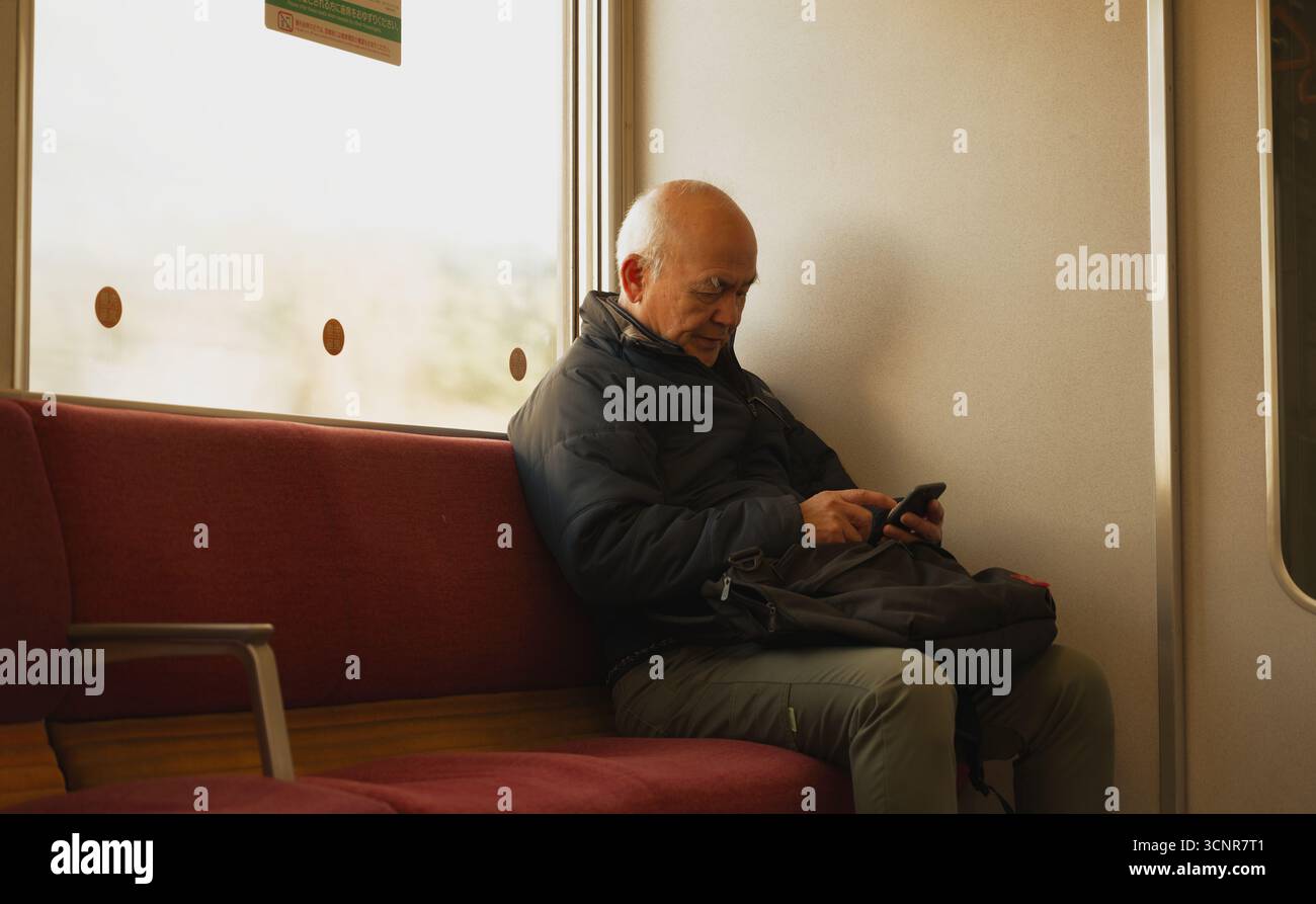 Homme âgé absorbé dans son téléphone pendant un trajet en train tranquille à travers la campagne de Nara Banque D'Images