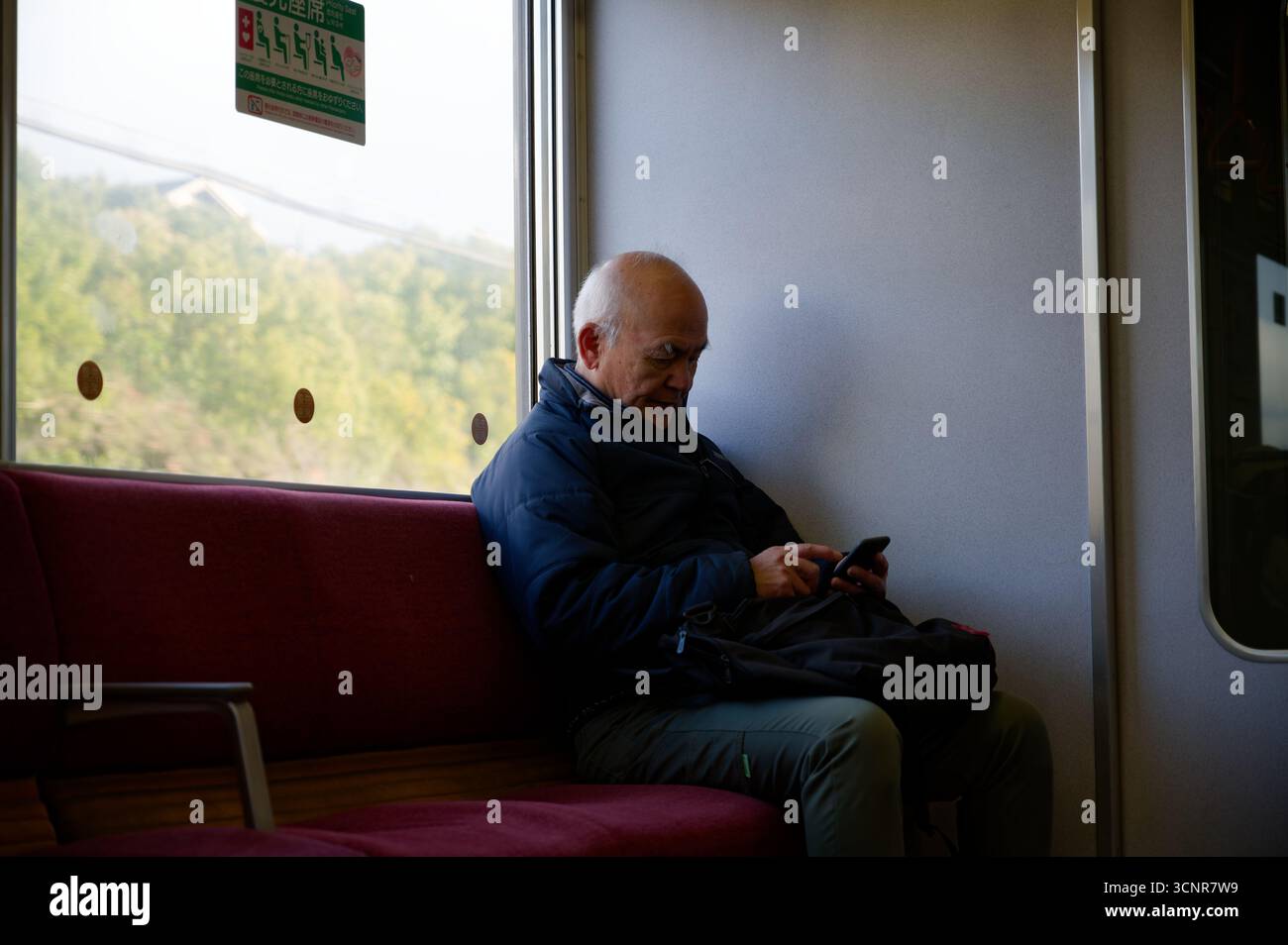 Homme japonais âgé absorbé dans son téléphone pendant un trajet en train tranquille à travers la campagne de Nara Banque D'Images