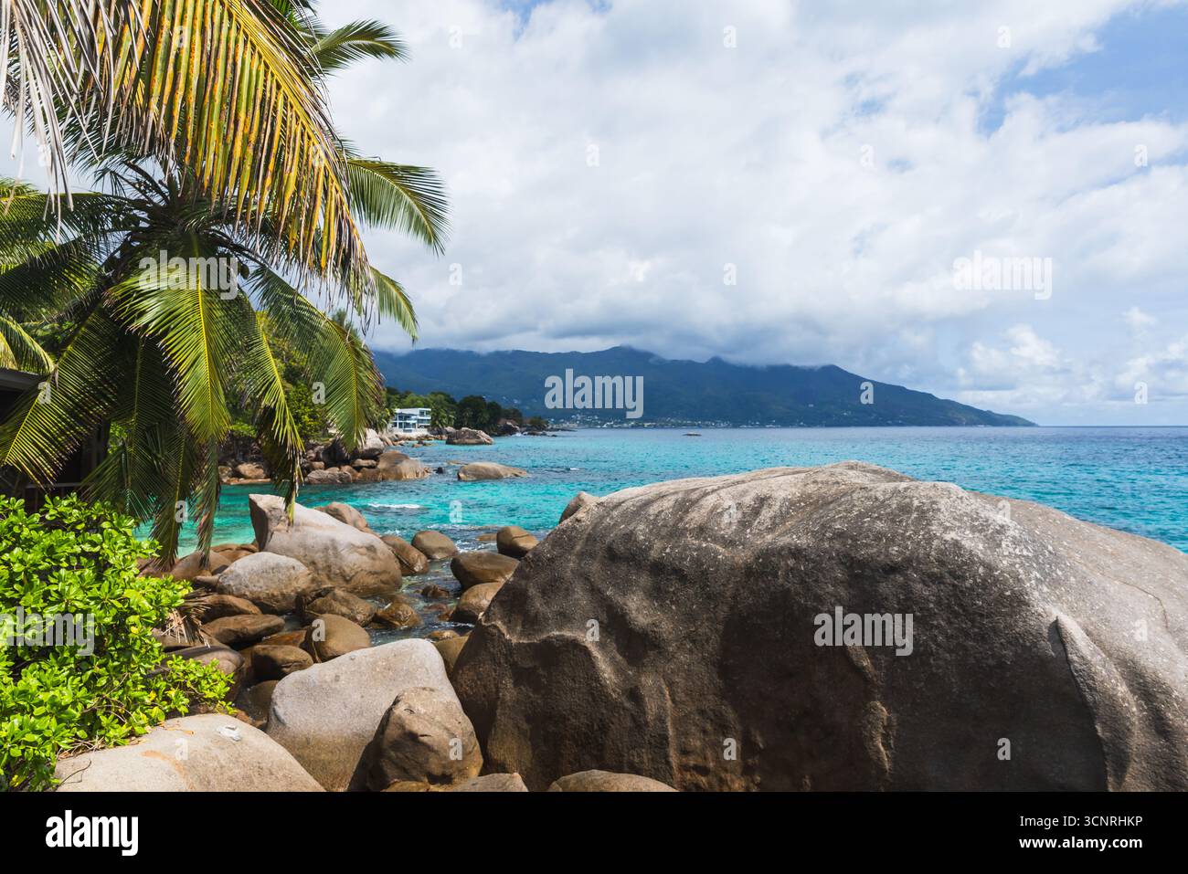 Paysage côtier tranquille avec palmiers, rochers de granit et eaux bleues. Un paysage tropical serein sous un ciel nuageux offrant détente a Banque D'Images Paysage côtier tranquille avec palmiers, rochers de granit et eaux bleues. Un paysage tropical serein sous un ciel nuageux offrant détente a Banque D'Images