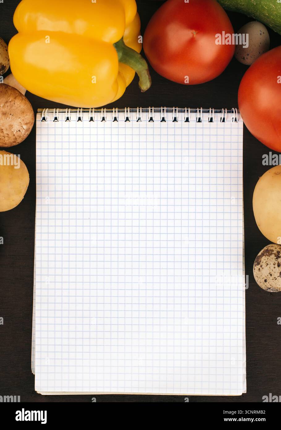 Cahier vierge entouré de divers légumes frais et œufs de caille sur un fond sombre Banque D'Images