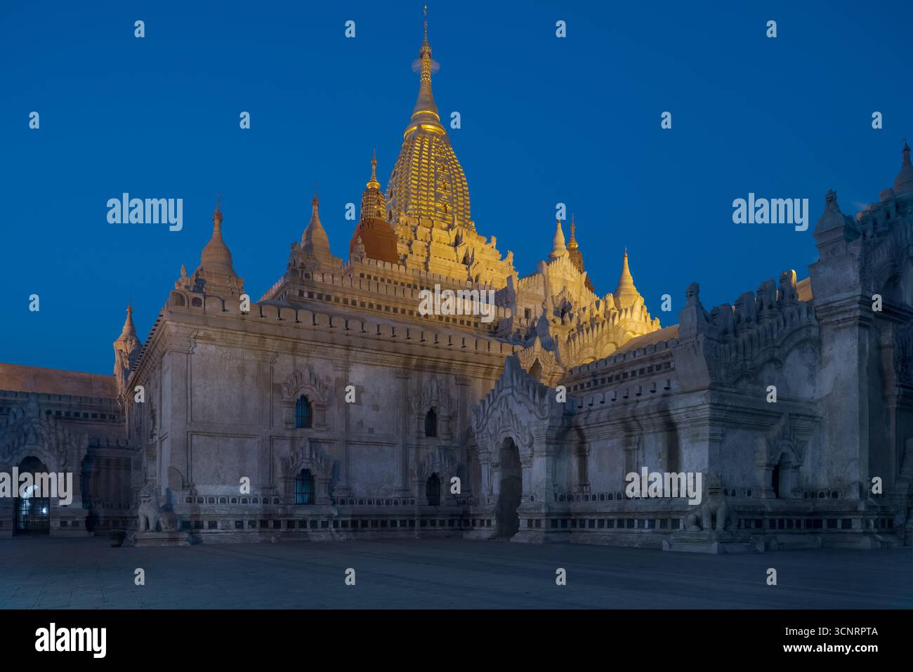 Temple Ananda bouddhiste illuminé à Bagan au crépuscule, ancienne architecture du Myanmar éclatant sous le ciel bleu profond du soir Banque D'Images