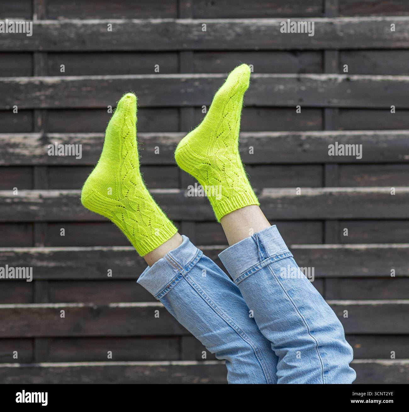 Une paire de pieds portant des chaussettes jaune fluo vif est surélevée, mettant en valeur le motif tricoté détaillé. La toile de fond présente des planches de bois rustiques, cre Banque D'Images