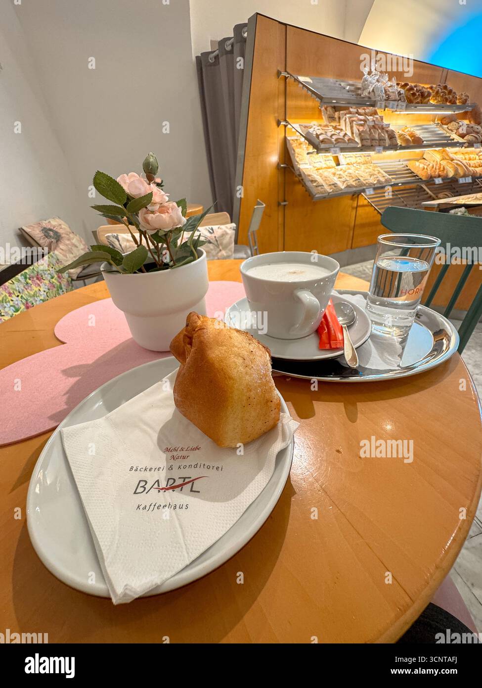 Un petit-déjeuner autrichien traditionnel dans une boulangerie locale confortable, avec pâtisserie fraîche, cappuccino et eau sur une table en bois. Banque D'Images